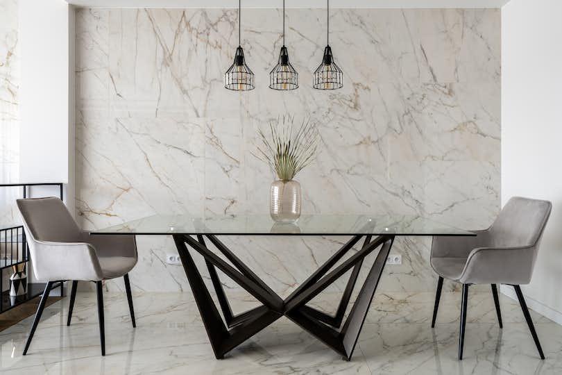 Stylish dining room with marble tiles on wall and floor and big, modern glass table with two chairs