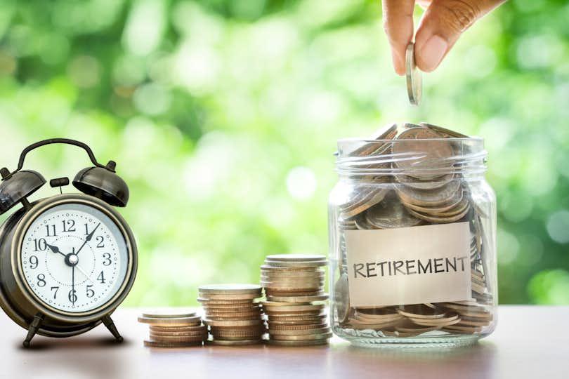 Hand putting Coins in glass jar for with retro alarm clock for time to money saving for retirement concept gen x retirement